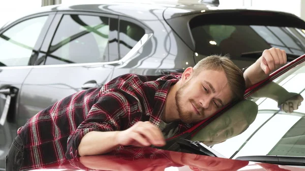 Feliz hombre acariciando su nuevo coche suavemente sonriendo mostrando pulgares hacia arriba en el concesionario —  Fotos de Stock