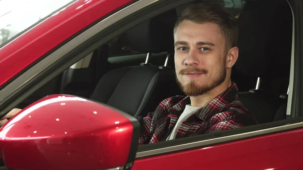Красивый молодой человек, удобно сидящий в своей новой машине и улыбающийся в камеру — стоковое фото