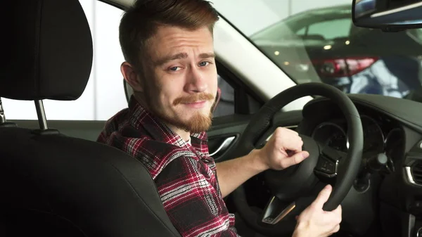 Atractivo hombre barbudo sonriendo a la cámara sobre su hombro sentado en un coche nuevo — Foto de Stock