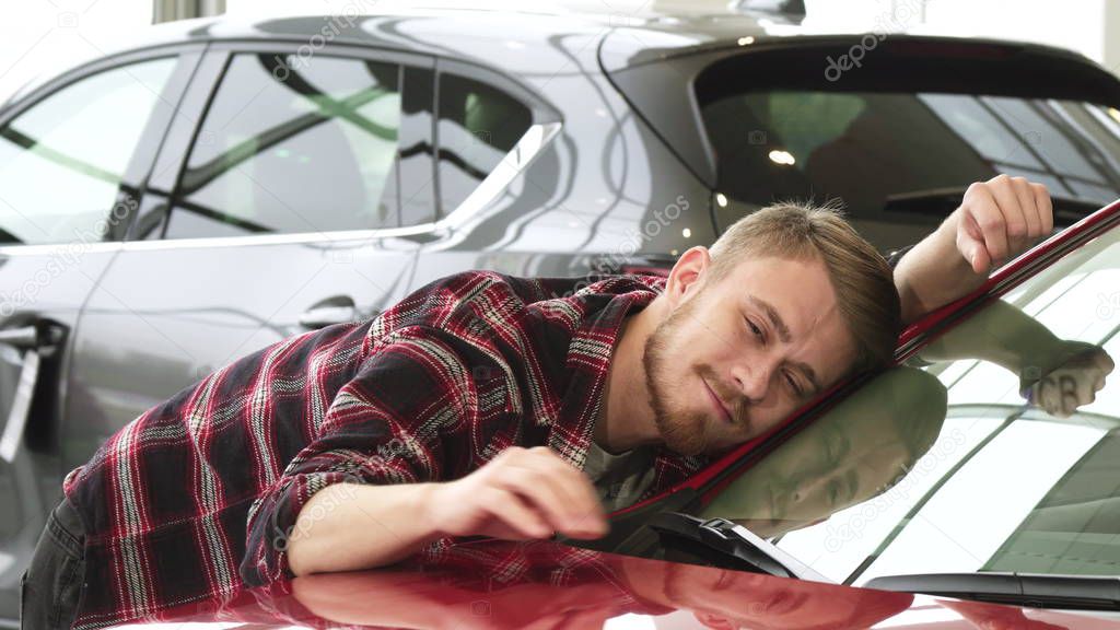 Happy man stroking his new car gently smiling showing thumbs up at the dealership