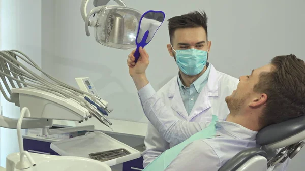 O paciente olha para os dentes no espelho no consultório do dentista. — Fotografia de Stock