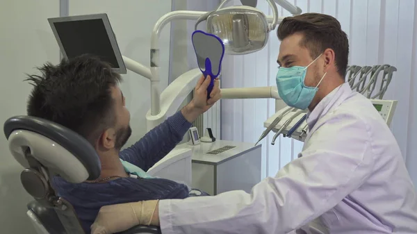 Patient looks into the mirror at the dentists office — Stock Photo, Image