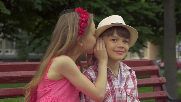 Little girl shares secrets with boy on the bench — Stock Photo, Image