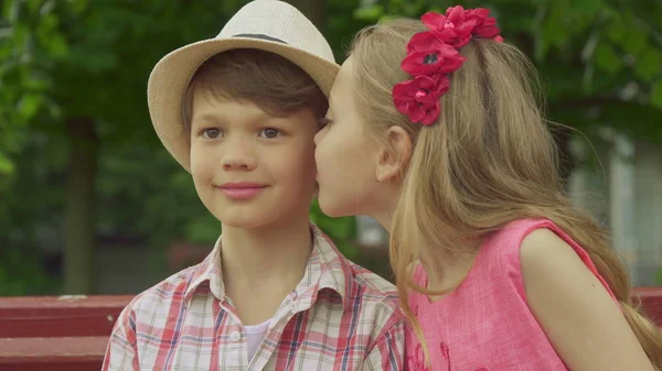 Niña besos chicos mejilla en el banco — Foto de Stock