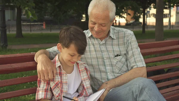 Little boy writes in his notebook what his grandpa says — Stock Photo, Image