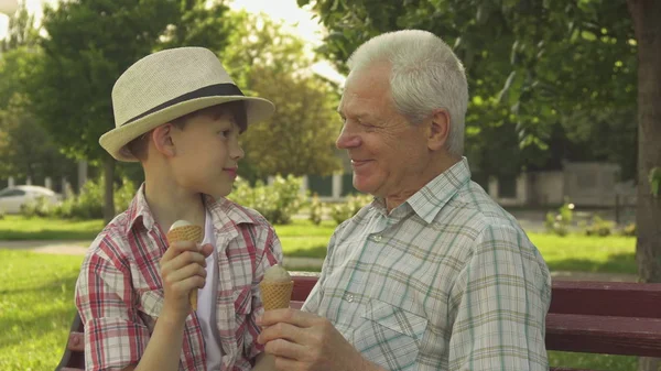Старший мужчина и его внук едят мороженое на скамейке — стоковое фото