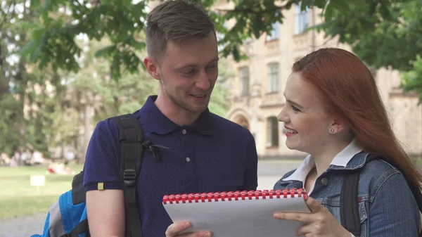Female student asks her classmate about something in notebook on campus — Stock Photo, Image