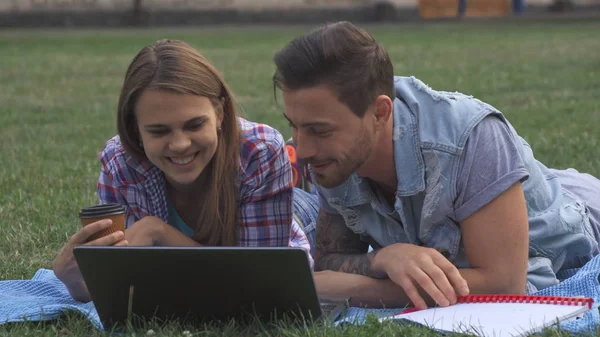 Two students discuss something on laptop on the lawn