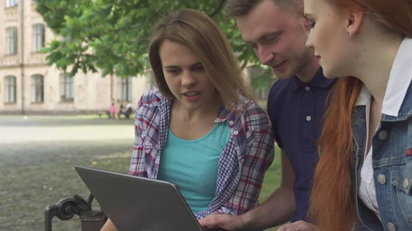 Uczniowie spojrzeć na laptopa na ławce — Zdjęcie stockowe