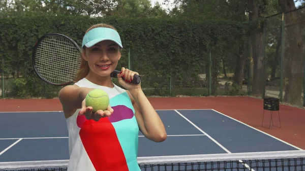 Menina com uma raquete sorrindo e oferecendo uma bola de tênis para câmera — Fotografia de Stock