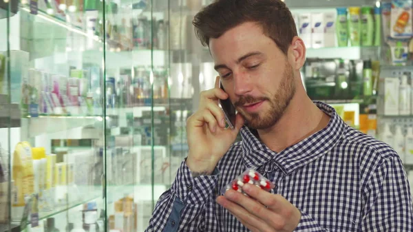 Homem falando ao telefone sobre pílulas na farmácia — Fotografia de Stock