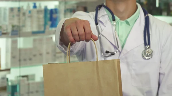 Médico sorrindo e segurando um pacote na farmácia — Fotografia de Stock