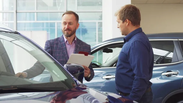 El vendedor en el traje muestra al cliente el interior del coche — Foto de Stock