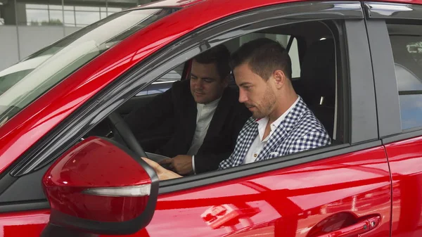 El vendedor y el comprador están sentados dentro del coche nuevo — Foto de Stock