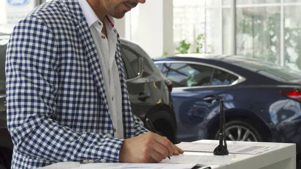 Серьезный покупатель подписывает документы на покупку автомобиля — стоковое фото