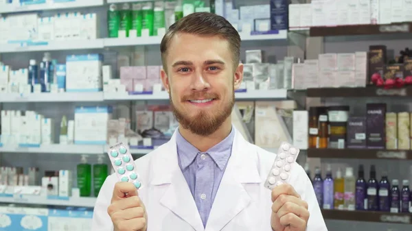 Jovem farmacêutico mostrando medicação e sorrindo — Fotografia de Stock
