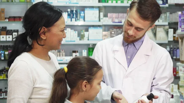 Um jovem farmacêutico fala sobre um dos produtos de farmácia para seus clientes — Fotografia de Stock