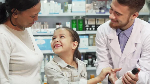 Farmacêutico amigável mostra menina um dos tubos — Fotografia de Stock