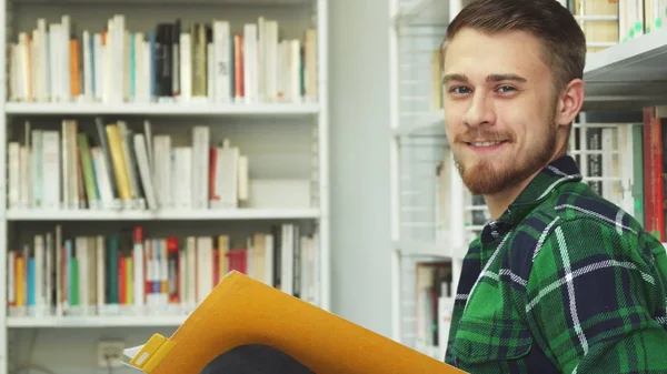 A laughing guy is sitting in the library and reading — Stock Photo, Image