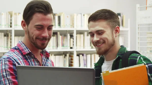 Двоє молодих студентів сміються стоячи в бібліотеці — стокове фото