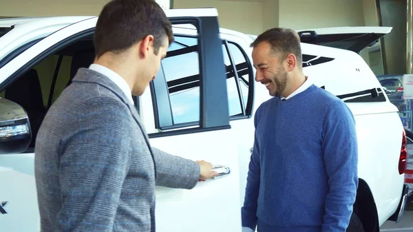 Elegante vendedor abre la puerta del coche e invita allí comprador — Foto de Stock
