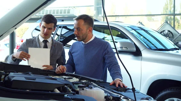 Un comprador y vendedor atento están estudiando los detalles en el capó abierto del coche — Foto de Stock