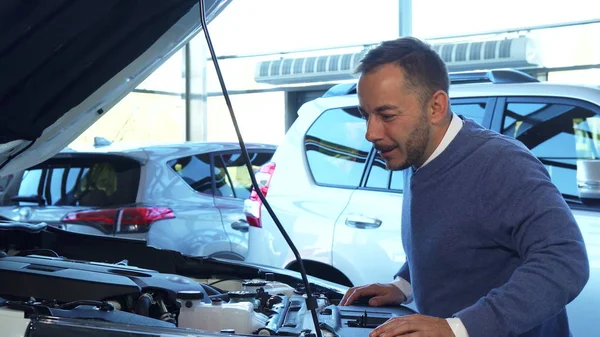 Un hombre alegre abrió la capucha del coche y estudió lo que hay dentro. — Foto de Stock