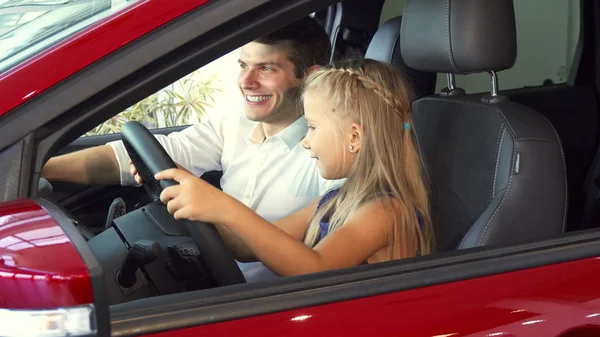 Una niña está sentada con su padre en el coche y fingiendo girar el volante — Foto de Stock