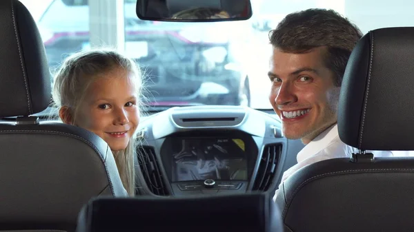 Divertido papá con su hija sentarse en los asientos delanteros y mirar la pequeña pantalla del coche — Foto de Stock