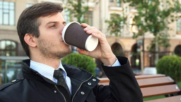 Un joven se sienta en un banco y bebe café. —  Fotos de Stock