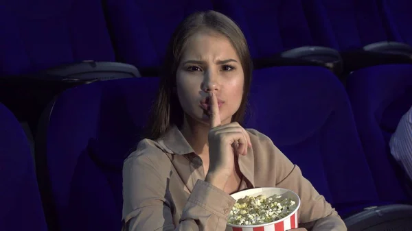 Девушка показывает знак молчания сидя в кинозале — стоковое фото