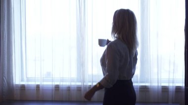 Zarif bir kız pencerenin kenarında duruyor ve kahve içiyor