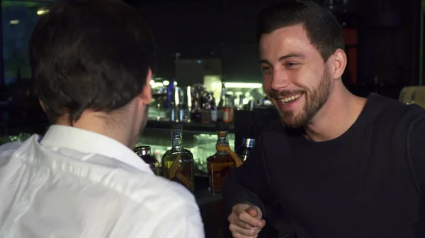 Young male friends talking while having drinks together at the bar