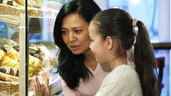 Мама и дочь делают покупки в пекарне, выбирают кондитерские изделия на витрине — стоковое фото