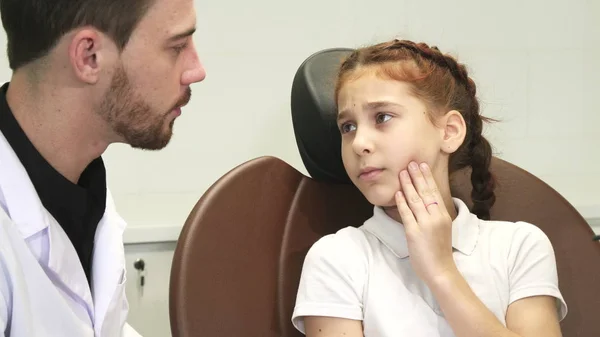 Uma menina triste descreve sua dor de dente para o médico — Fotografia de Stock