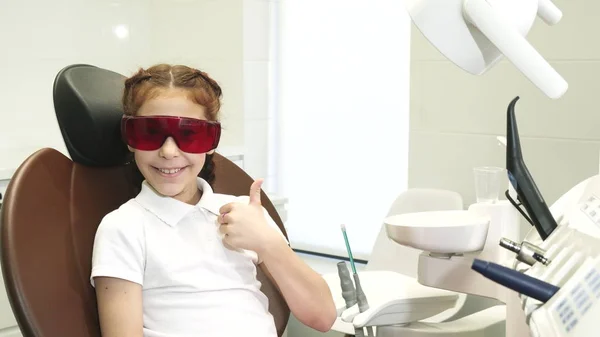 Menina feliz na recepção no dentista mostra um polegar para cima — Fotografia de Stock