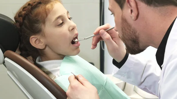 Um médico profissional examina cuidadosamente os dentes de uma menina — Fotografia de Stock