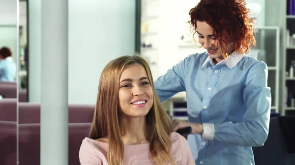 Happy young woman getting her hair combed by professional hairdresser at the salon — Stock Photo, Image