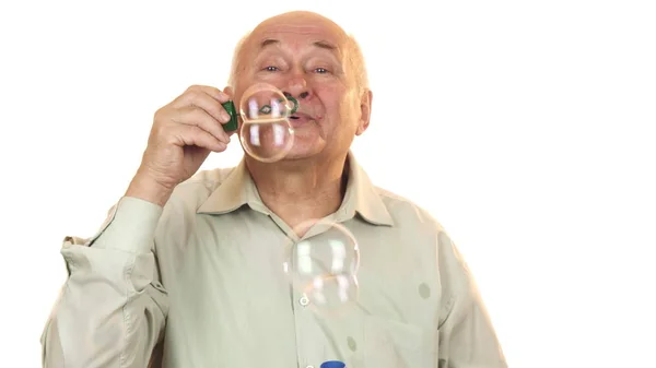Hombre alegre mayor soplando burbujas aisladas en blanco — Foto de Stock
