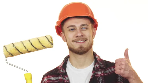 Feliz joven constructor masculino sosteniendo rodillo de pintura mostrando los pulgares hacia arriba — Foto de Stock