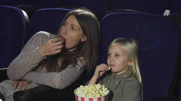 Beautiful woman and her little daughter eating popcorn watching movie at the cinema — Stock Photo, Image
