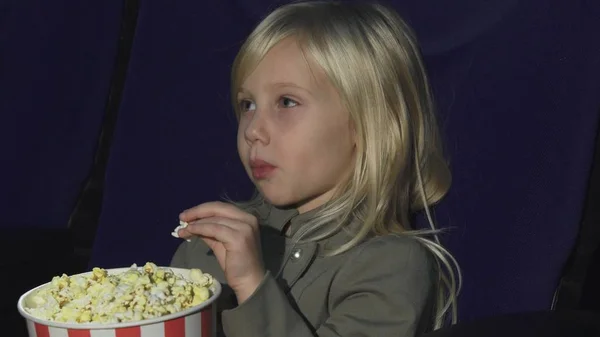 Close up of an adorable little girl eating popcorn while at the movie theatre — Stock Photo, Image