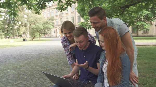 Quatro estudantes riem do que vêem no laptop no campus — Fotografia de Stock