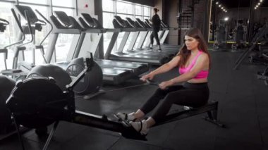 Güzel kıvrımlı sporcu spor salonunda kürek makinesi üzerinde çalışıyor