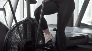 Güzel kıvrımlı kadın spor salonunda hava bisikleti üzerinde kardiyo yapıyor kameraya gülümseyen