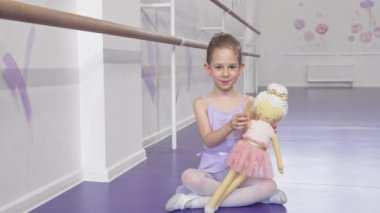 Bir bebek ile oynarken kameraya sallayarak güzel bir küçük balerin tam uzunlukta çekim