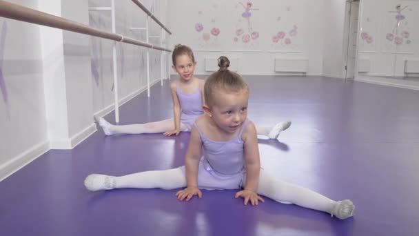 Two cute little ballerinas girls stretching at ballet class doing splits — Stock Video
