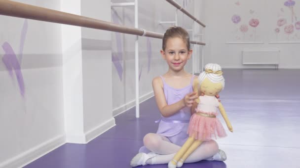 Bir bebek ile oynarken kameraya sallayarak güzel bir küçük balerin tam uzunlukta çekim — Stok video
