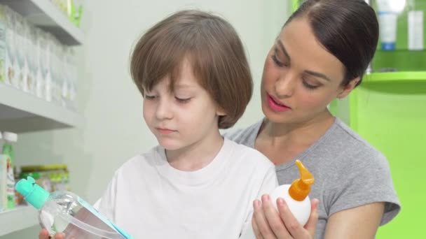 Schöne Frau und ihr Sohn wählen zwischen zwei Produkten in der Drogerie — Stockvideo