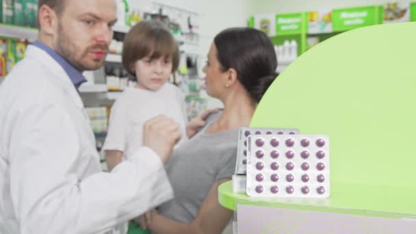 Фармацевт дає блістер з таблетками маленькому хлопчикові та його мамі — стокове відео